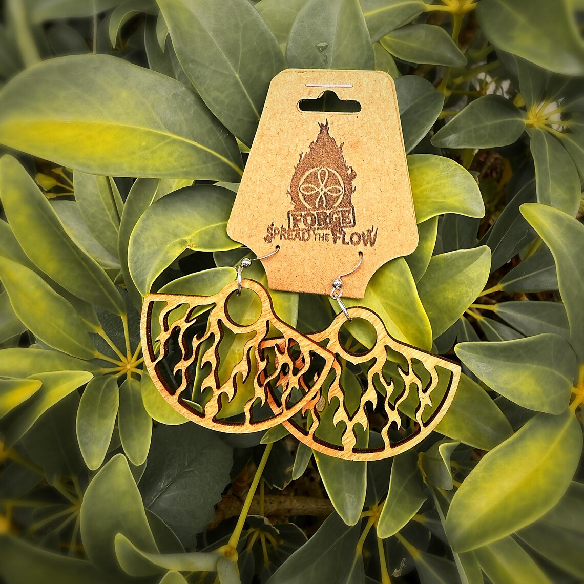 The EMBER fan earrings on their FORGE branded card, resting against green foliage