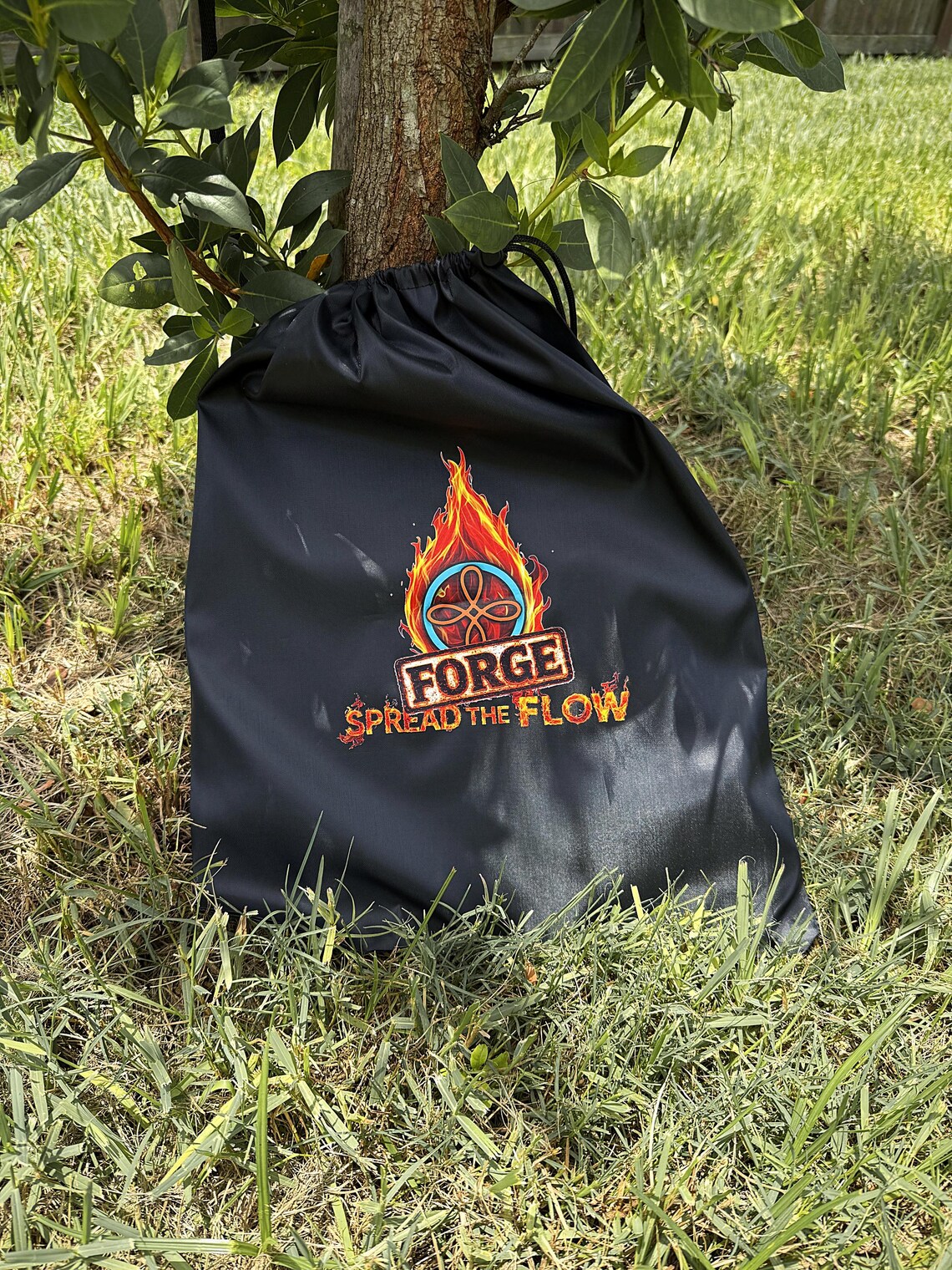 The black FORGE drawstring carry bag that ships with every pair, resting against a tree