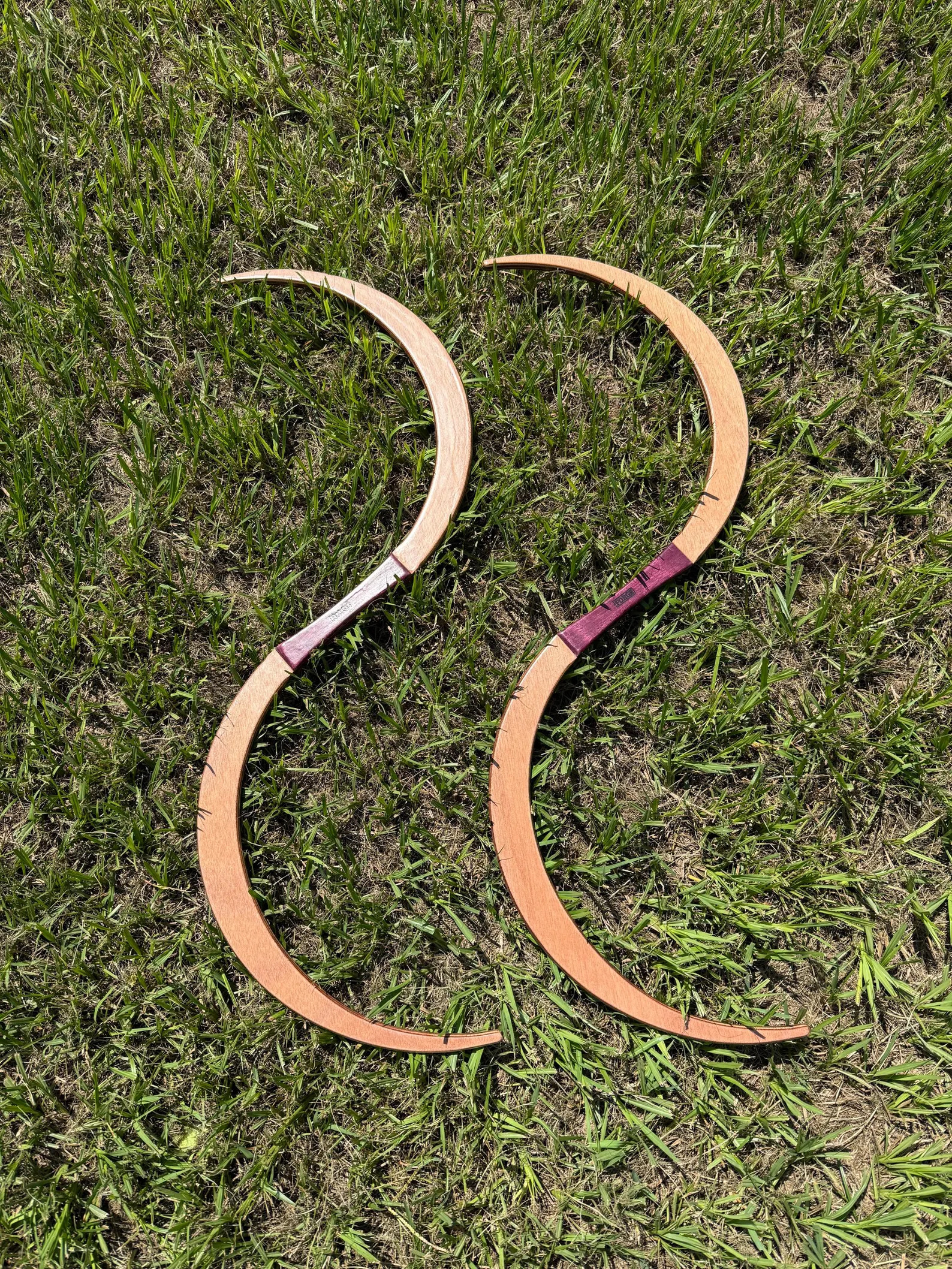 A pair of TruGENG S-staves in okoume with Purpleheart grips, laid on grass