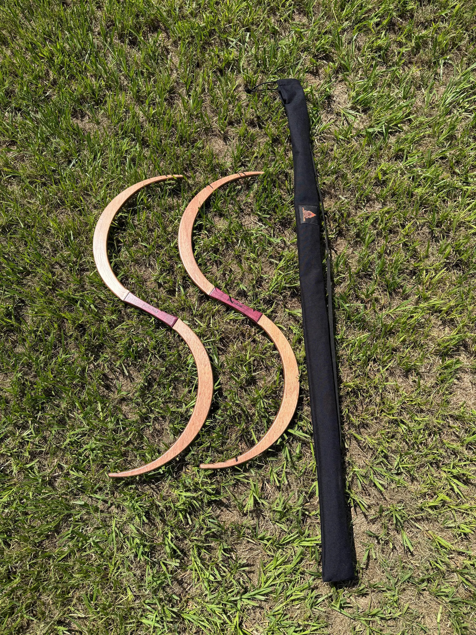 A pair of TruGENG S-staves curved into an S-shape on the grass beside their black FORGE carry bag